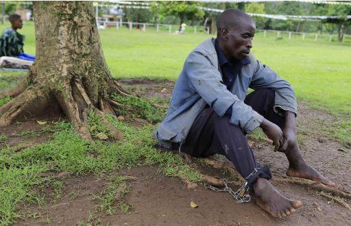 A man who is mentally ill and chained to a tree waits for healing prayers by Omukama Ruhanga Owobusobozi Bisaka, an 83-year-old self-professed god and founder of the Ugandan cult group Faith of Unity, at the cult's headquarters in Kapyemi village