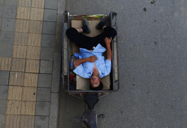 A man takes a nap on his tricycle during a hot day in Beijing