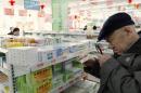 An elderly man uses a magnifier to see the descriptions on a pack of medicine at a pharmacy in Dandong