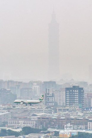 由於大陸冷氣團帶來境外汙染物，16日全台大部分地區PM2.5達到「紫爆」等級，一架民航機正飛越霧茫茫的台北上空，遠方101大樓幾乎消失在霧霾中（郭吉銓攝）。