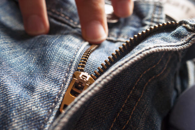 Fingers on Button and Elements of Denim Blue Jeans Metal Zipper.