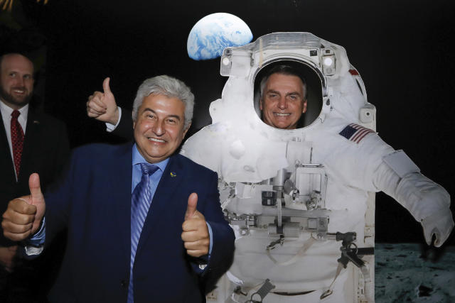 In this handout photo released by Brazil's Presidential Press Office, Brazil's President Jair Bolsonaro poses for a photo standing behind a life size cardboard cutout of a U.S. astronaut, alongside the Minister of Science and Technology Marcos Cesar Pontes, during a private event at the U.S. Embassy celebrating the July 4th Independence Day and the upcoming 50th anniversary of the Apollo 11 moonwalk, in Brasilia, Brazil. (Carolina Antunes/Brazil's Presidential Press Office via AP)