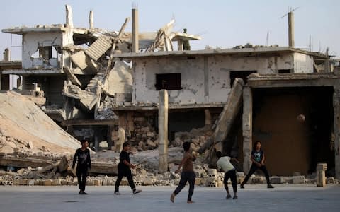 Children play football in front of a damaged building in a rebel-held neighbourhood of Deraa in southern Syria - Credit: AFP